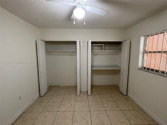 unfurnished bedroom with ceiling fan, light tile patterned floors, a textured ceiling, and two closets