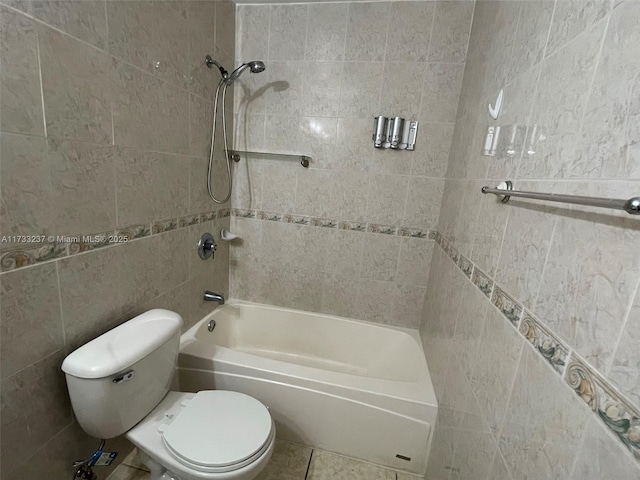 bathroom featuring tiled shower / bath, toilet, and tile walls