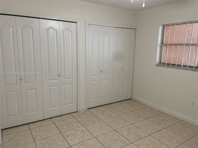 unfurnished bedroom featuring light tile patterned floors and two closets