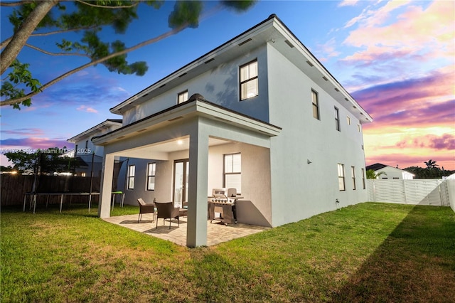 back house at dusk featuring a yard, a trampoline, and a patio area