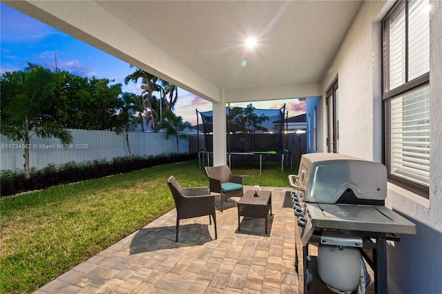 patio terrace at dusk featuring a trampoline, a grill, and a lawn