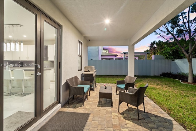 patio terrace at dusk with french doors, outdoor lounge area, and a lawn