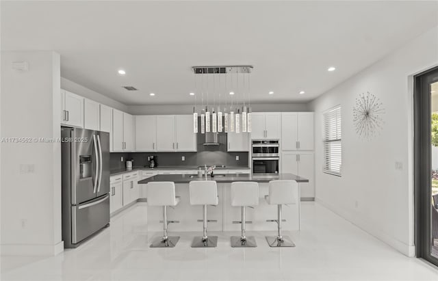 kitchen with a breakfast bar area, a kitchen island with sink, hanging light fixtures, white cabinetry, and stainless steel appliances