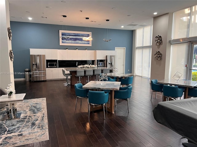 dining area with dark hardwood / wood-style flooring, expansive windows, and a high ceiling