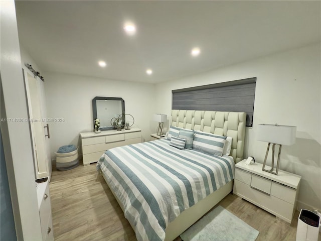 bedroom with a barn door and light hardwood / wood-style flooring