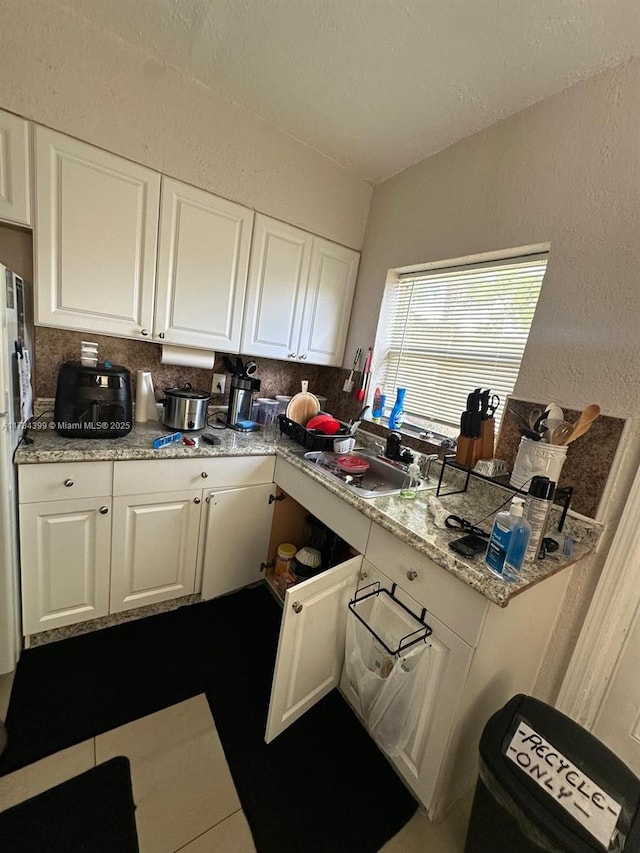 kitchen featuring sink, white cabinets, backsplash, tile patterned flooring, and light stone countertops