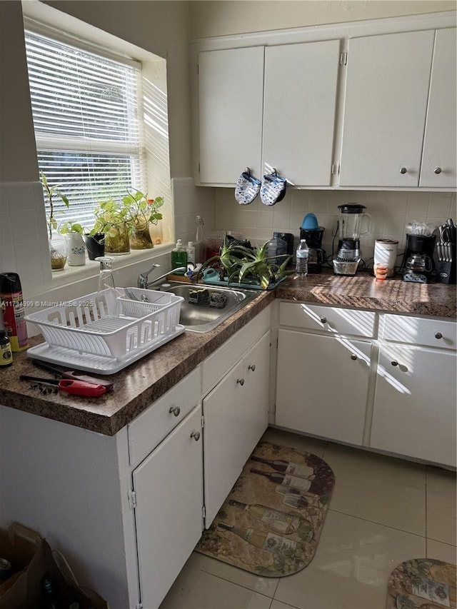 kitchen with tasteful backsplash, sink, light tile patterned floors, and white cabinets