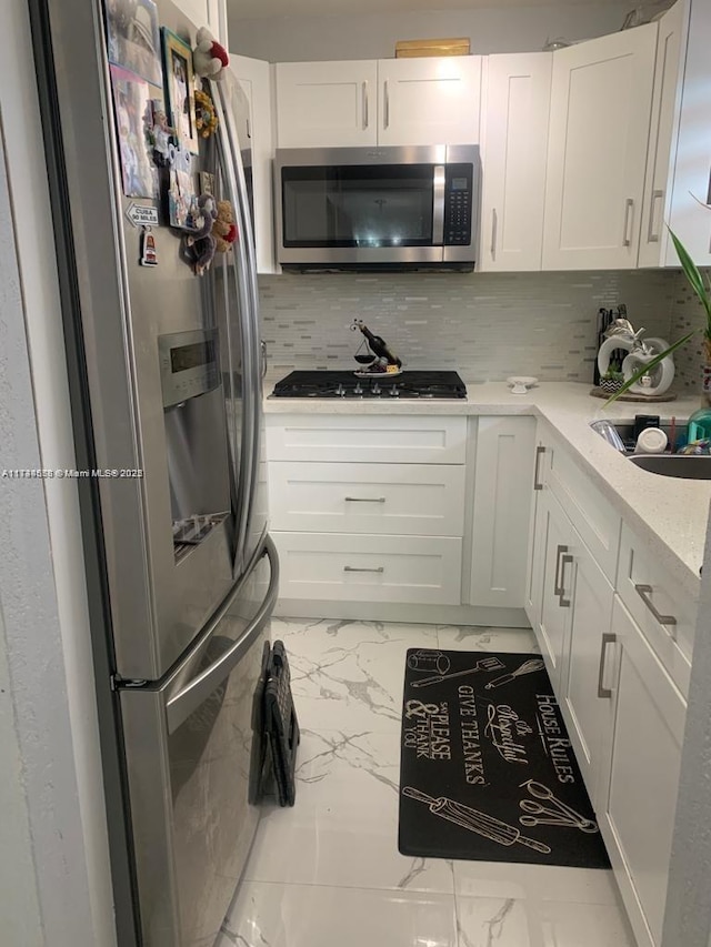 kitchen featuring sink, white cabinetry, stainless steel appliances, light stone countertops, and backsplash