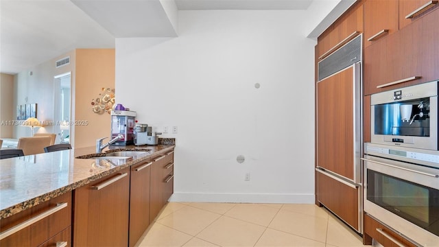 kitchen featuring sink, paneled built in refrigerator, light stone counters, light tile patterned flooring, and stainless steel double oven