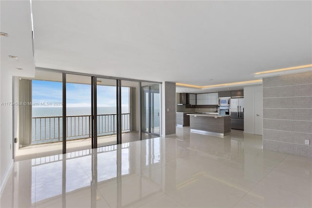 unfurnished living room featuring light tile patterned flooring, floor to ceiling windows, and a water view