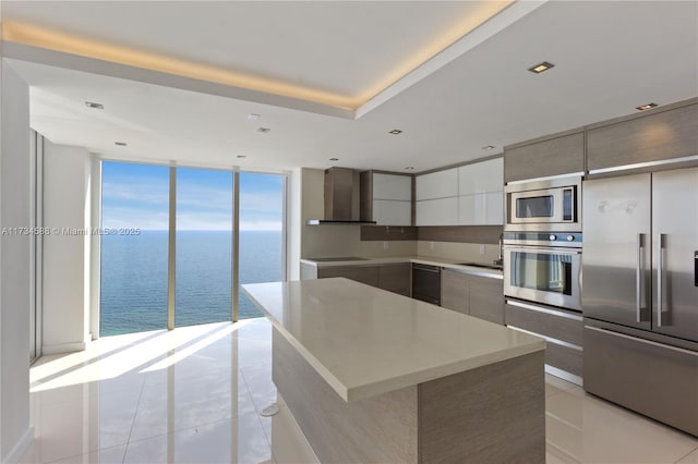 kitchen with a water view, built in appliances, a center island, light tile patterned floors, and expansive windows