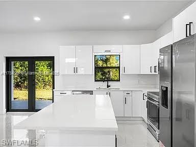 kitchen featuring stainless steel appliances, sink, white cabinets, a healthy amount of sunlight, and backsplash