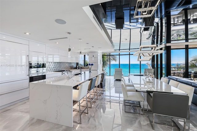 kitchen with white cabinetry, a spacious island, a water view, decorative light fixtures, and stainless steel double oven