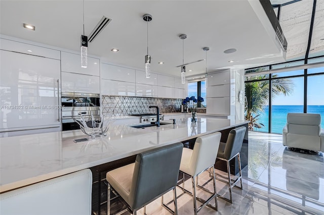 kitchen featuring decorative light fixtures, white cabinetry, sink, a breakfast bar area, and a water view