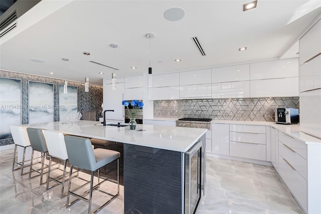 kitchen featuring pendant lighting, white cabinetry, a center island with sink, a kitchen bar, and beverage cooler