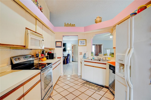 kitchen featuring sink, a textured ceiling, light tile patterned floors, appliances with stainless steel finishes, and white cabinets