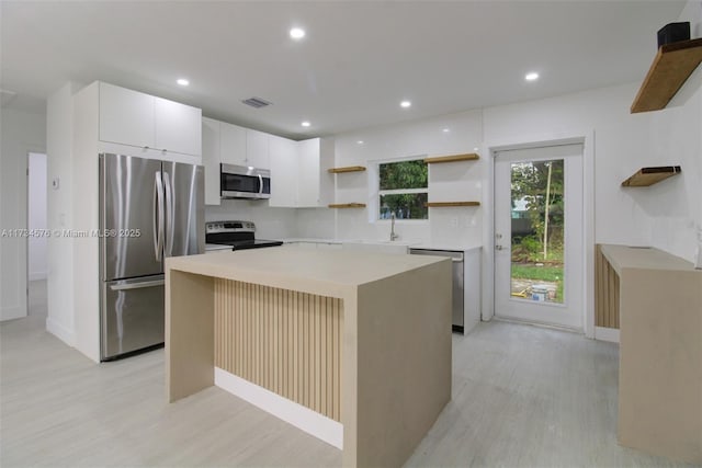 kitchen featuring sink, white cabinetry, light hardwood / wood-style flooring, a kitchen island, and stainless steel appliances