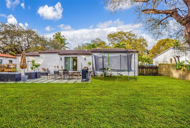 rear view of property with a patio, a trampoline, and a lawn