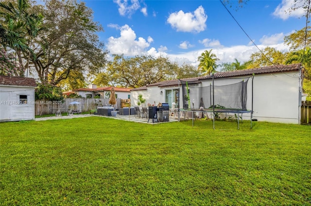 rear view of property with a trampoline, a storage shed, a yard, and a patio area