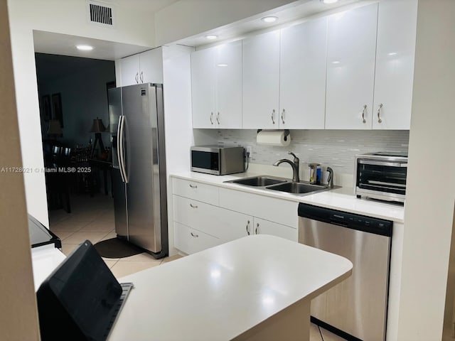 kitchen with light tile patterned flooring, appliances with stainless steel finishes, tasteful backsplash, sink, and white cabinets