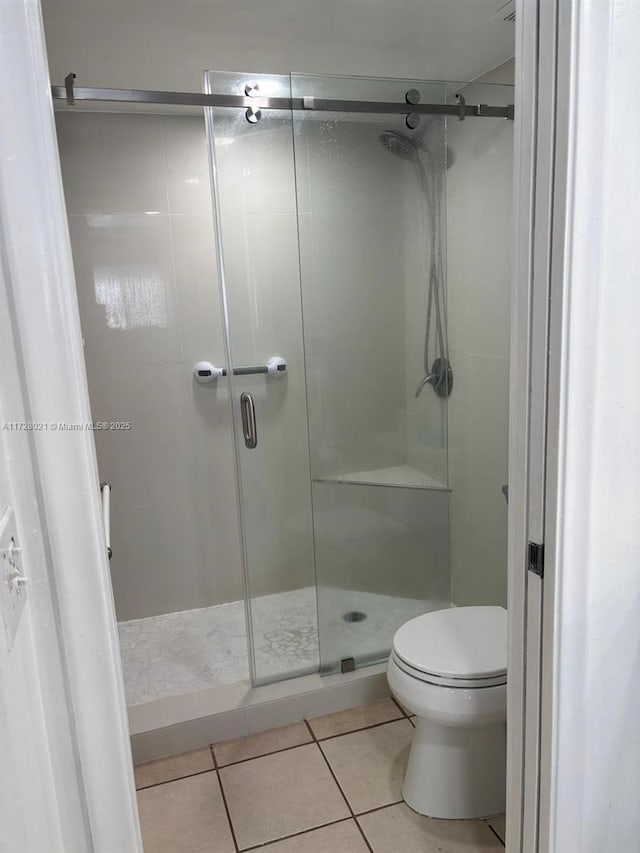 bathroom with toilet, a shower with shower door, and tile patterned flooring