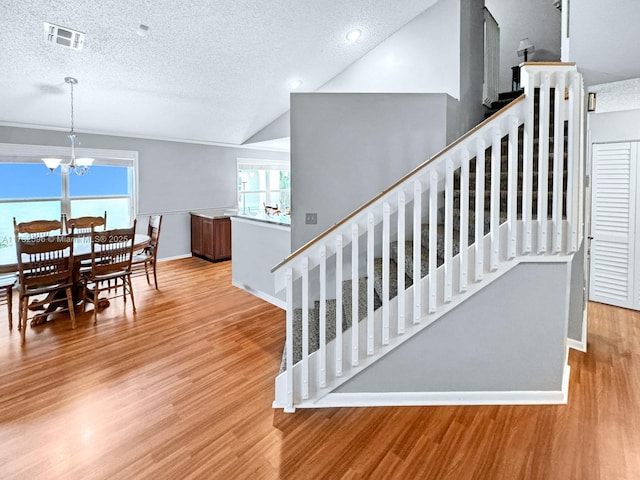 stairway featuring vaulted ceiling, a chandelier, hardwood / wood-style floors, and a textured ceiling