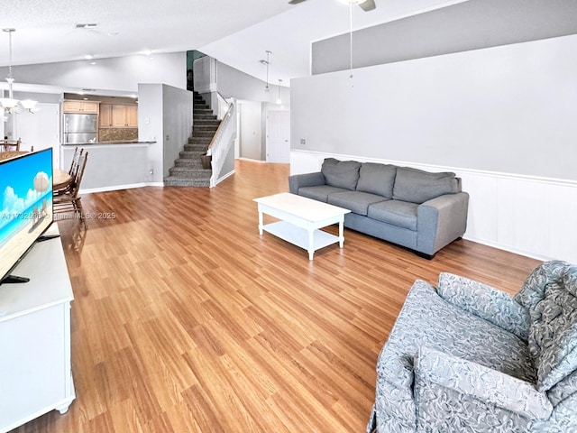 living room featuring ceiling fan with notable chandelier, vaulted ceiling, a textured ceiling, and light wood-type flooring