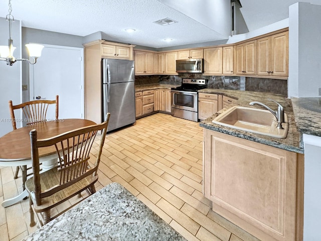 kitchen with sink, hanging light fixtures, a textured ceiling, appliances with stainless steel finishes, and kitchen peninsula