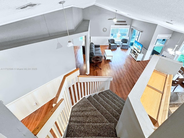 staircase with ceiling fan, hardwood / wood-style flooring, vaulted ceiling, and a textured ceiling