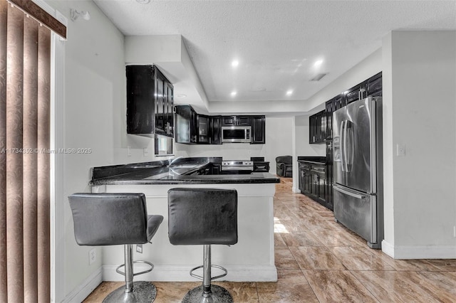 kitchen with stainless steel appliances, a breakfast bar, kitchen peninsula, and a textured ceiling