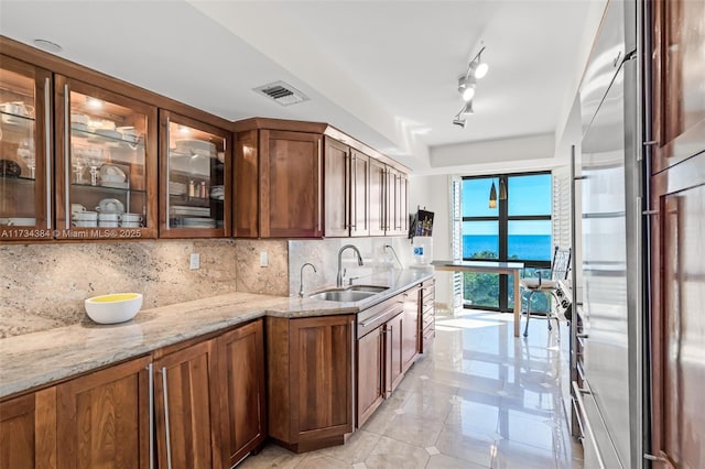 kitchen with sink, rail lighting, light stone counters, tasteful backsplash, and high end refrigerator