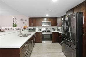 kitchen featuring sink, light hardwood / wood-style flooring, stainless steel appliances, dark brown cabinetry, and kitchen peninsula