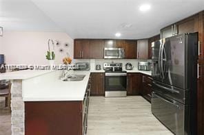 kitchen with sink, light hardwood / wood-style flooring, appliances with stainless steel finishes, a kitchen breakfast bar, and dark brown cabinetry