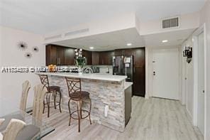 kitchen featuring dark brown cabinetry, a breakfast bar area, stainless steel fridge, kitchen peninsula, and light hardwood / wood-style floors