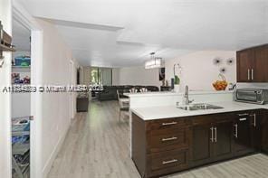 kitchen with light hardwood / wood-style floors, dark brown cabinetry, kitchen peninsula, and sink