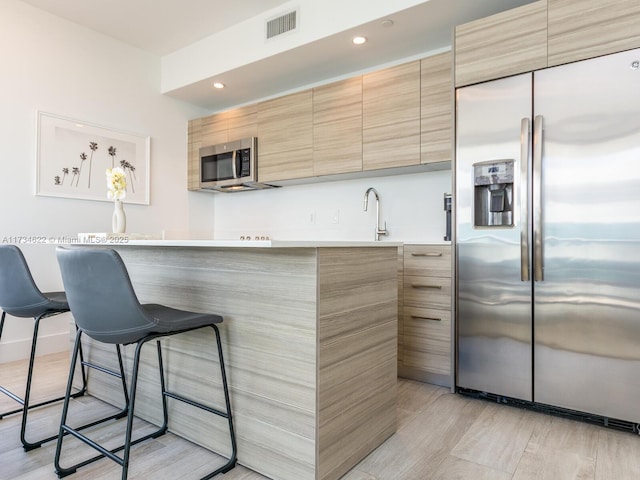 kitchen with stainless steel appliances, a kitchen breakfast bar, and light brown cabinets