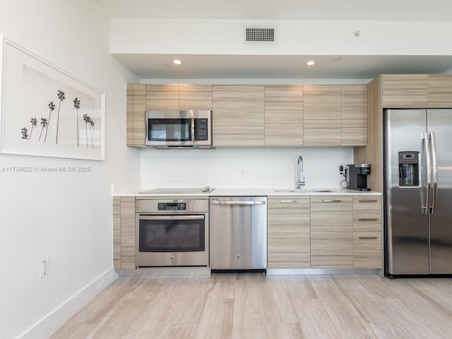 kitchen featuring appliances with stainless steel finishes, sink, light brown cabinets, and light hardwood / wood-style flooring