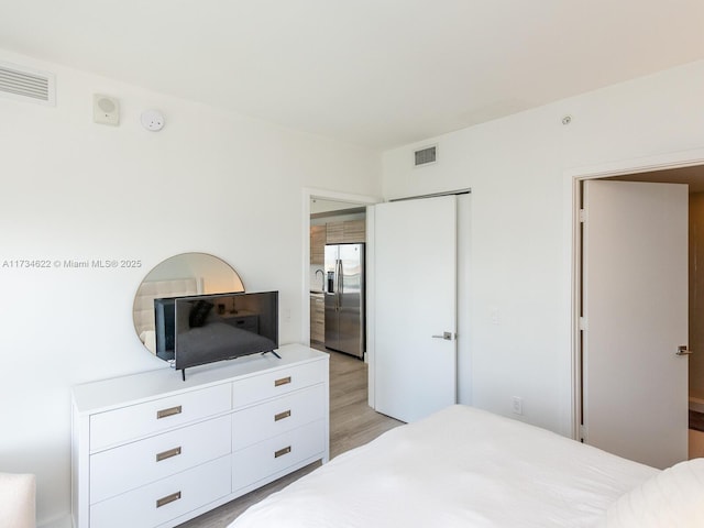 bedroom with stainless steel fridge with ice dispenser, light hardwood / wood-style floors, and a closet