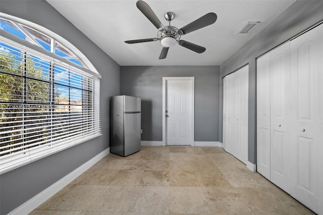 unfurnished bedroom with ceiling fan, two closets, stainless steel fridge, and a textured ceiling