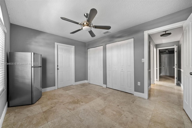 unfurnished bedroom featuring ceiling fan, a textured ceiling, stainless steel fridge, and multiple closets