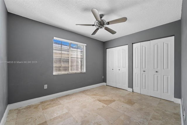 unfurnished bedroom with ceiling fan, a textured ceiling, and multiple closets