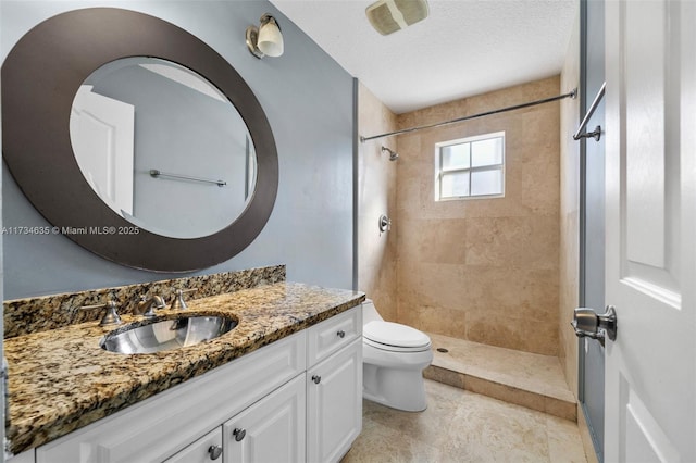 bathroom with vanity, toilet, a textured ceiling, and a tile shower