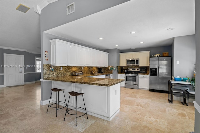 kitchen featuring appliances with stainless steel finishes, dark stone countertops, white cabinets, backsplash, and kitchen peninsula