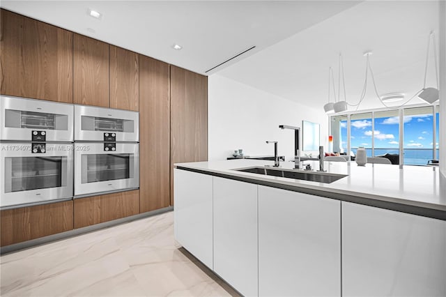 kitchen featuring double oven, sink, decorative light fixtures, and white cabinets