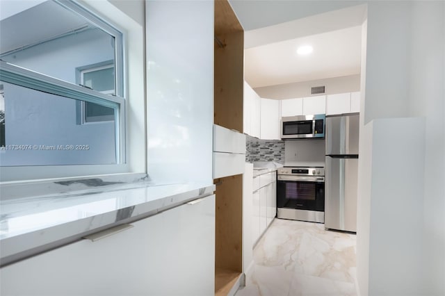 kitchen featuring stainless steel appliances, white cabinets, and backsplash