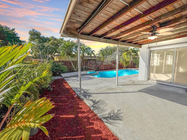 patio terrace at dusk with ceiling fan and a fenced in pool