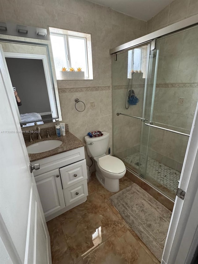 bathroom with a shower with door, tile walls, tile patterned flooring, vanity, and toilet