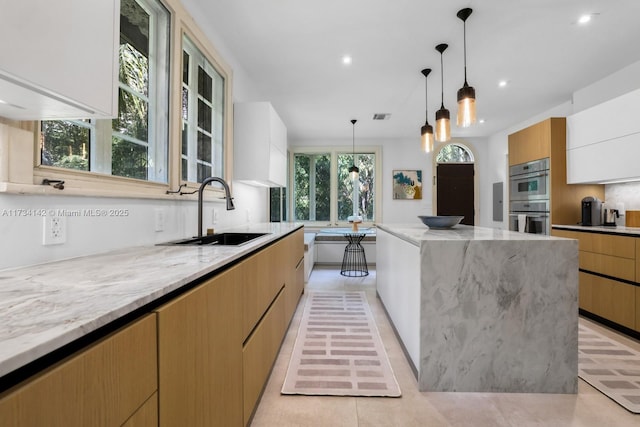 kitchen with sink, white cabinetry, decorative light fixtures, stainless steel double oven, and light stone countertops