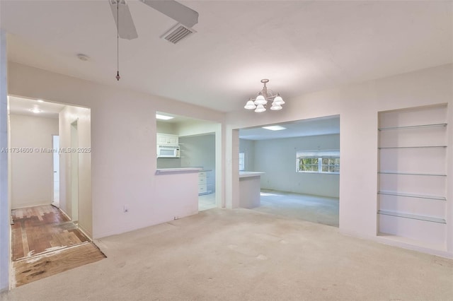 carpeted spare room featuring ceiling fan with notable chandelier