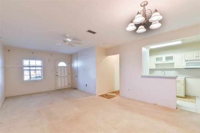 unfurnished living room featuring ceiling fan with notable chandelier and light colored carpet